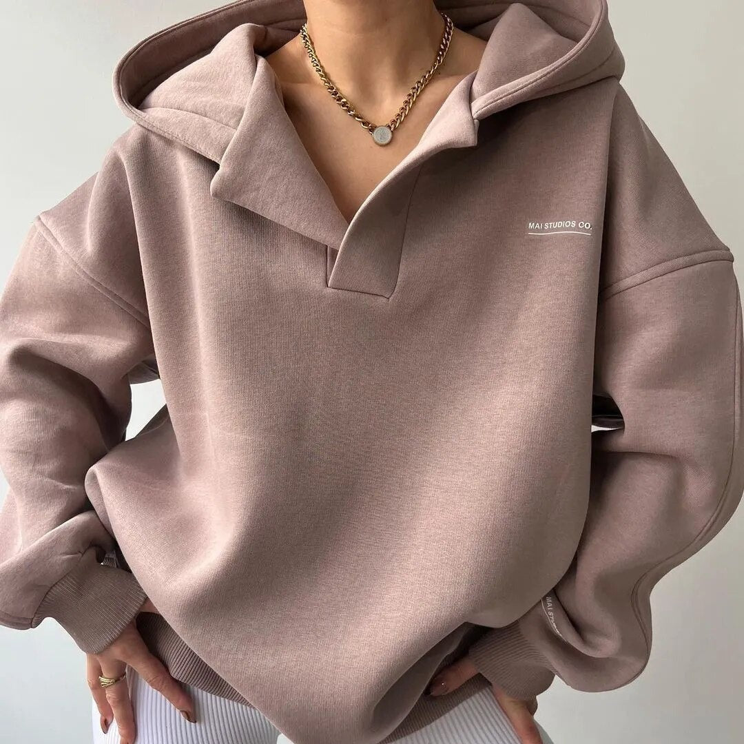 Person wearing a light brown hoodie with a small logo on a neutral background