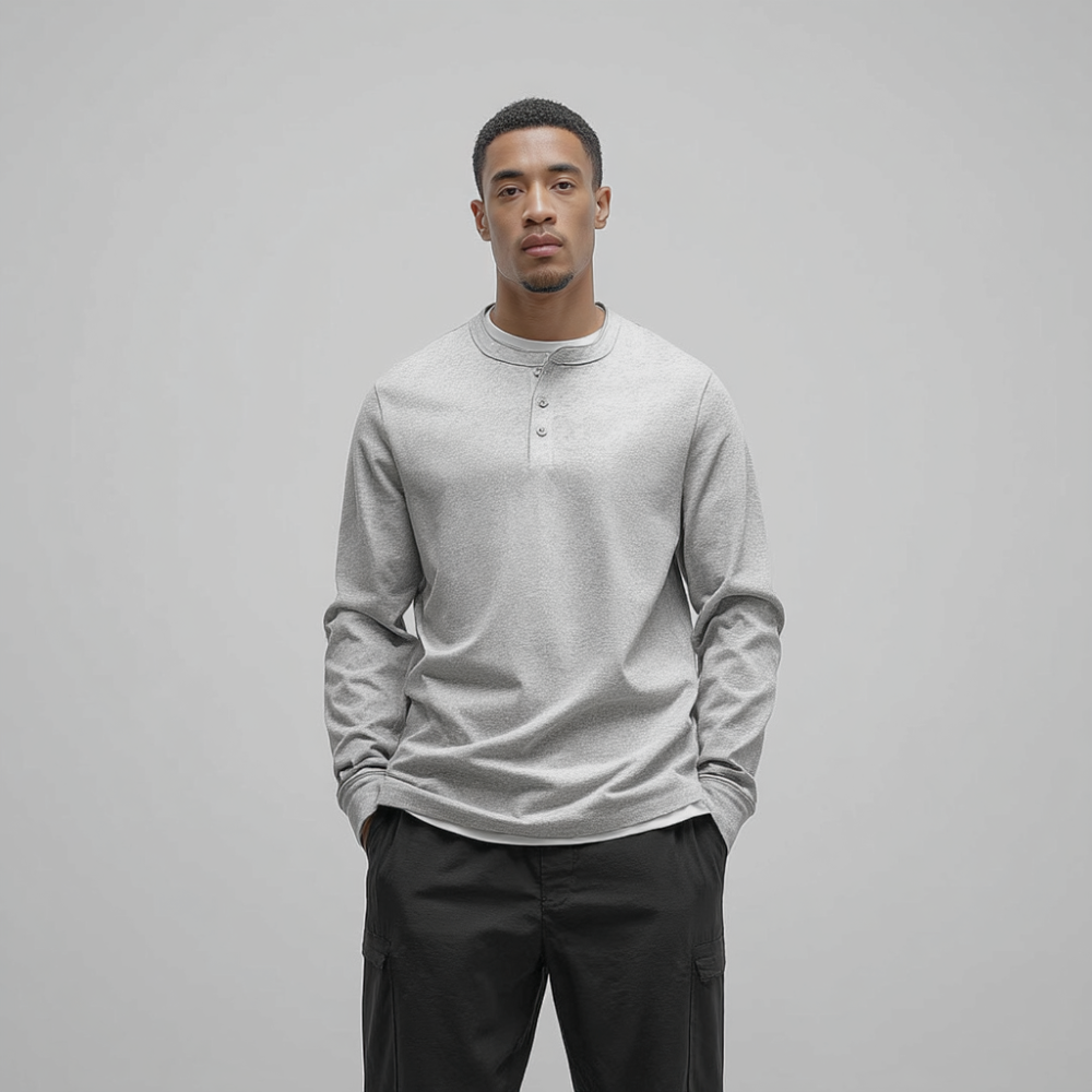 Man wearing a light gray long-sleeve shirt and dark pants against a plain background